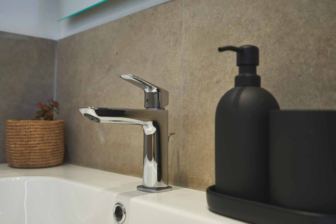 A bathroom with a chrome faucet, a black soap dispenser, and a woven basket on the counter.