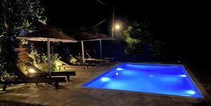 Ein Pool bei Nacht mit Liegestühlen und Sonnenschirmen.