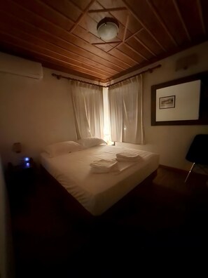 Ein Schlafzimmer mit Holzboden, einem Bett mit weißen Leinen, einer Nachttischlampe und einem gerahmten Bild an der Wand.