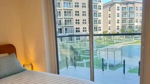 Quarto com uma cama grande, porta de vidro deslizante para uma varanda e vista para um prédio residencial.