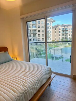 A bedroom with a large bed, a sliding glass door leading to a balcony, and a view of a residential building. - Apartamento frente al mar con vista a la piscina (punta chame)