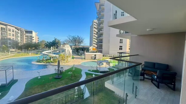 Varanda de hotel moderna com guarda-corpo de vidro, área de piscina com escorrega e vista para edifícios vizinhos.