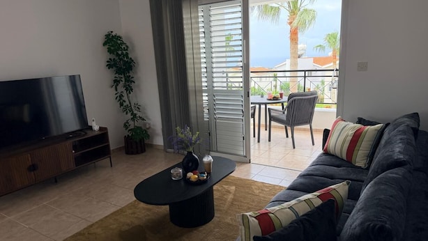 Ein Wohnzimmer mit Fernseher, Sofa, Couchtisch und einem Balkon mit Blick.