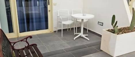 Eine Terrasse mit Bank, Tisch, Stühlen und einem Pflanzgefäß mit einem Kaktus.