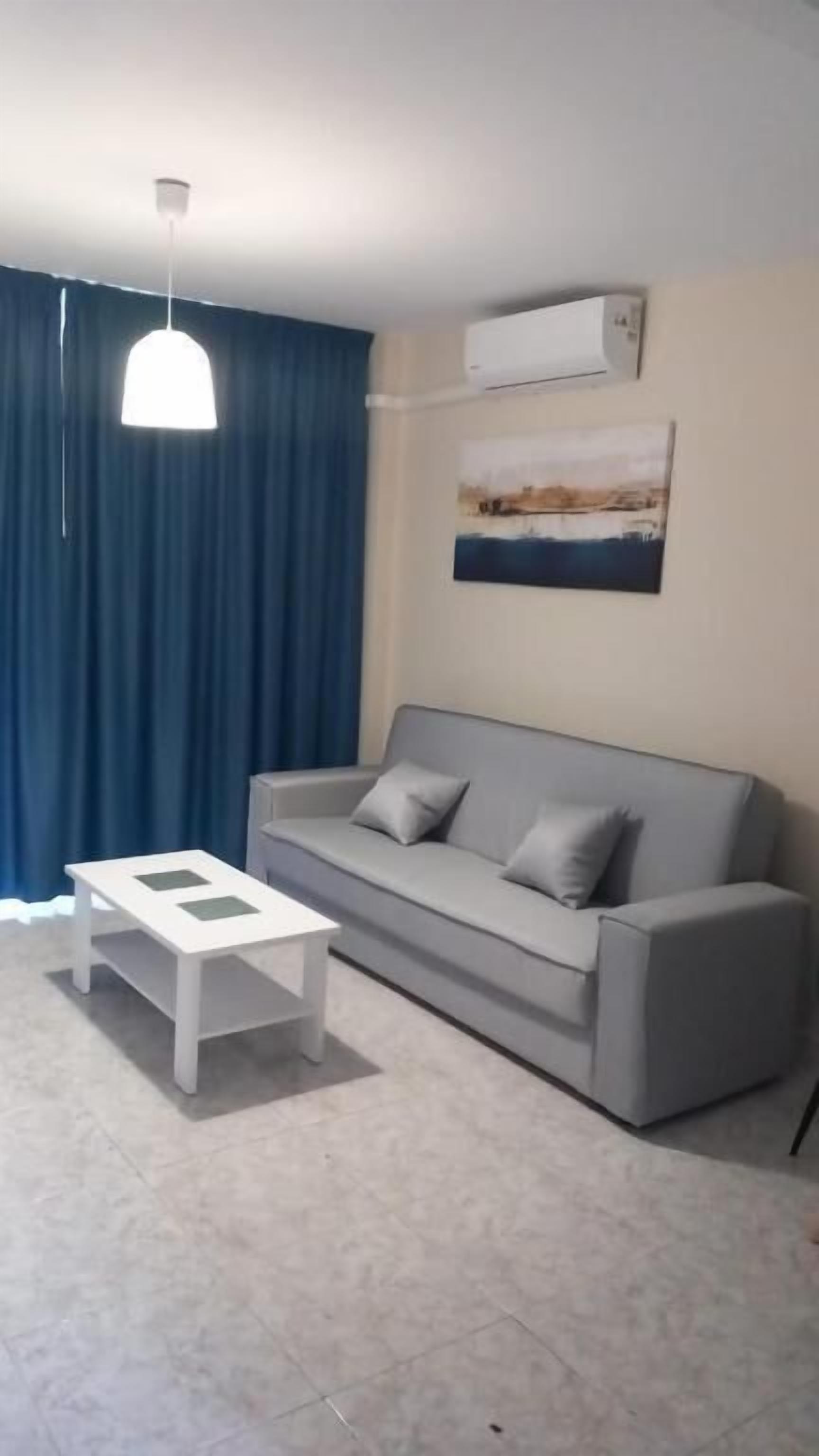 A living room with a grey sofa, a white coffee table, blue curtains, and a ceiling light fixture.