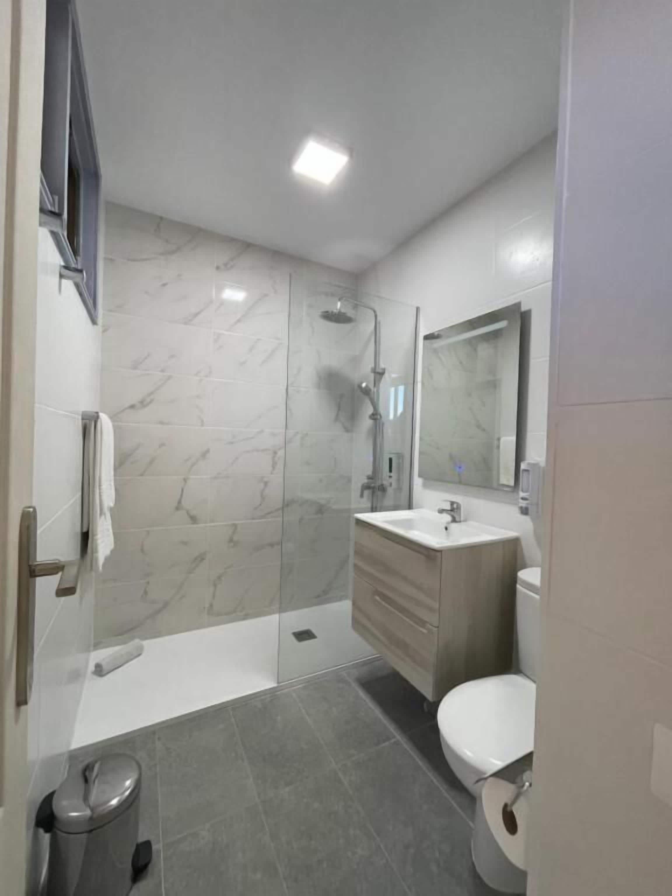 A modern bathroom with a glass shower enclosure, a white sink, and a toilet.