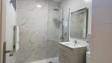 A modern bathroom with a glass shower enclosure, a white sink, and a toilet.