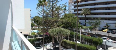 Un patio de hotel con mobiliario exterior, palmeras y un edificio de varios pisos al fondo.