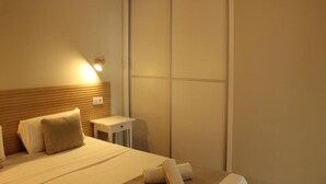 A hotel room with a bed, a bedside table, a wall-mounted light, and a sliding door. - Apartamentos Fayna (Gran Canarias)