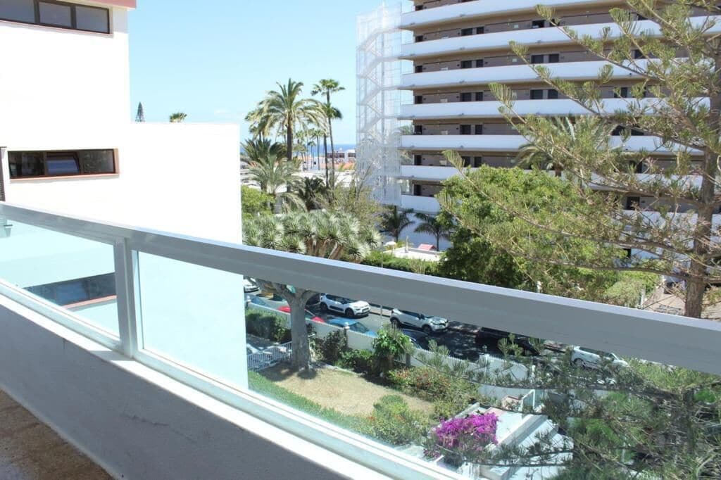 A residential building with a balcony, palm trees, and parked cars.