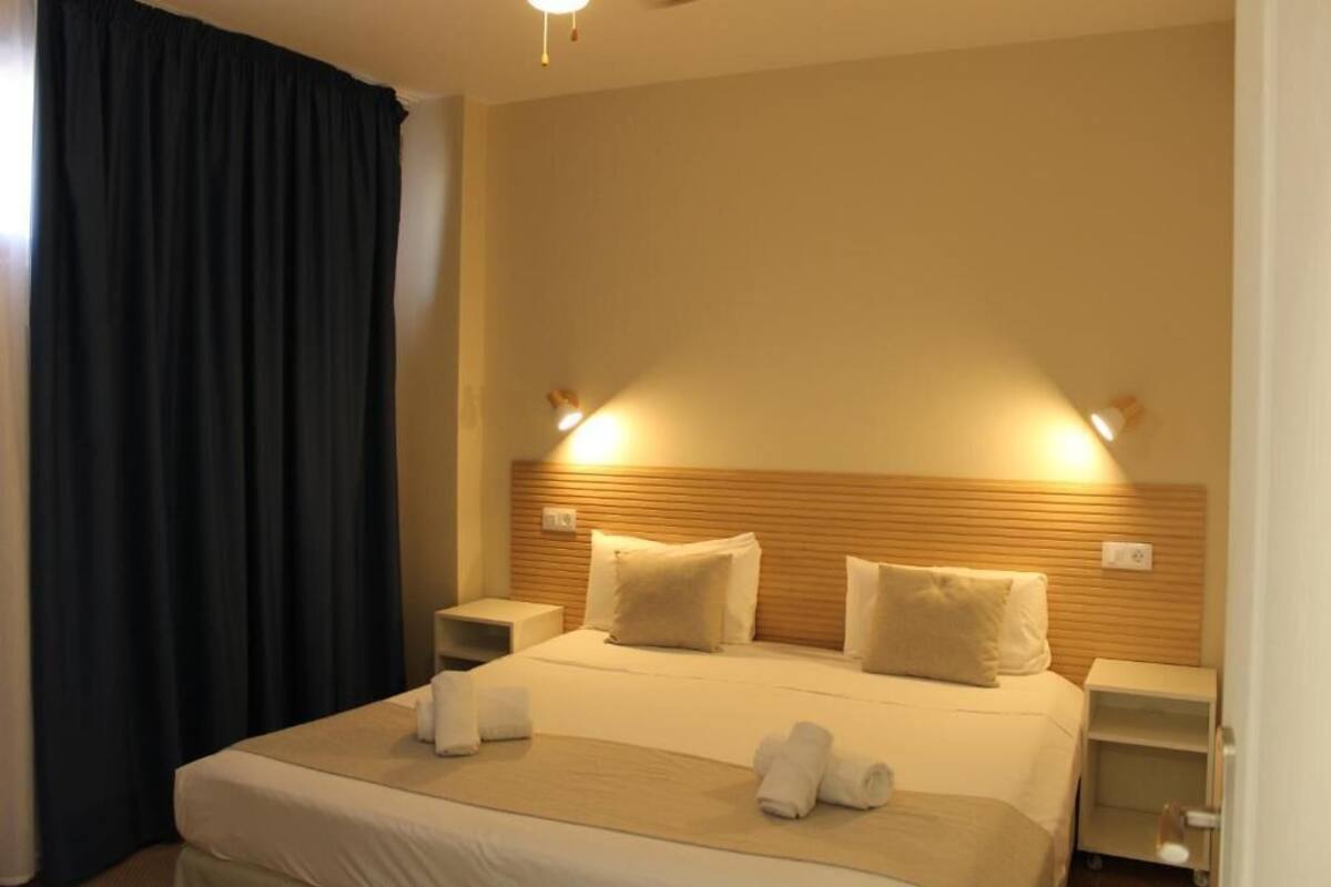 A hotel room with a bed, two bedside tables, a headboard, and a curtain.