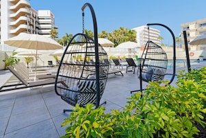 Area esterna con tavoli sotto ombrelloni, piscina e un edificio sullo sfondo.