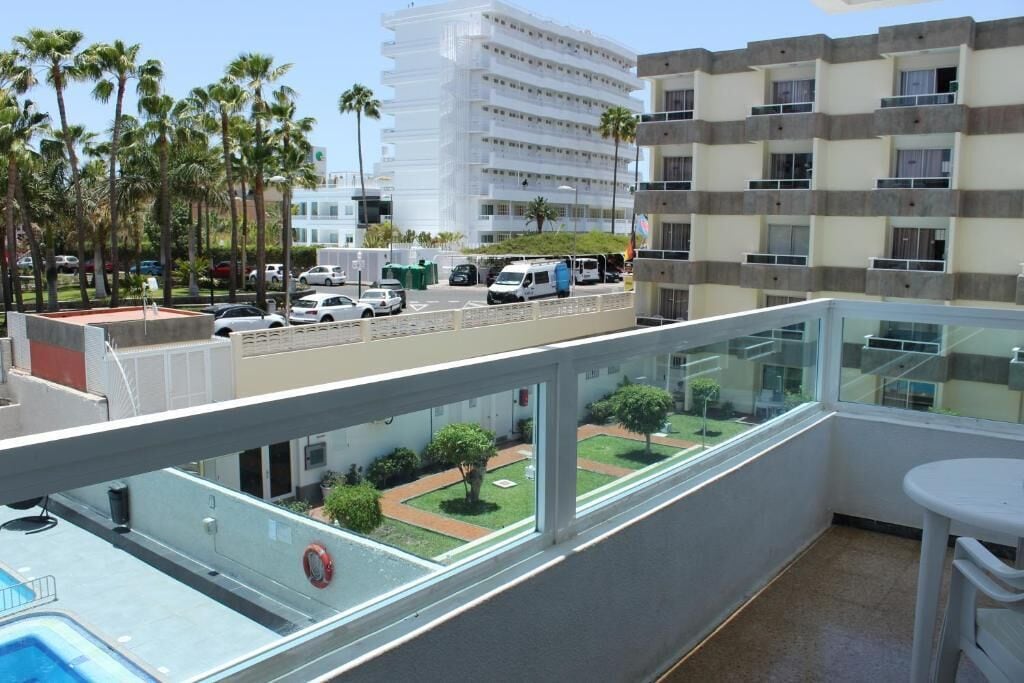 A balcony with a view of a street, a pool, and a building with multiple floors.