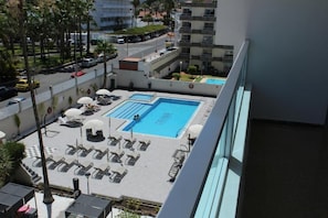 A rooftop pool with lounge chairs and umbrellas, surrounded by a high-rise building. - Apartamentos Fayna (Gran Canarias)