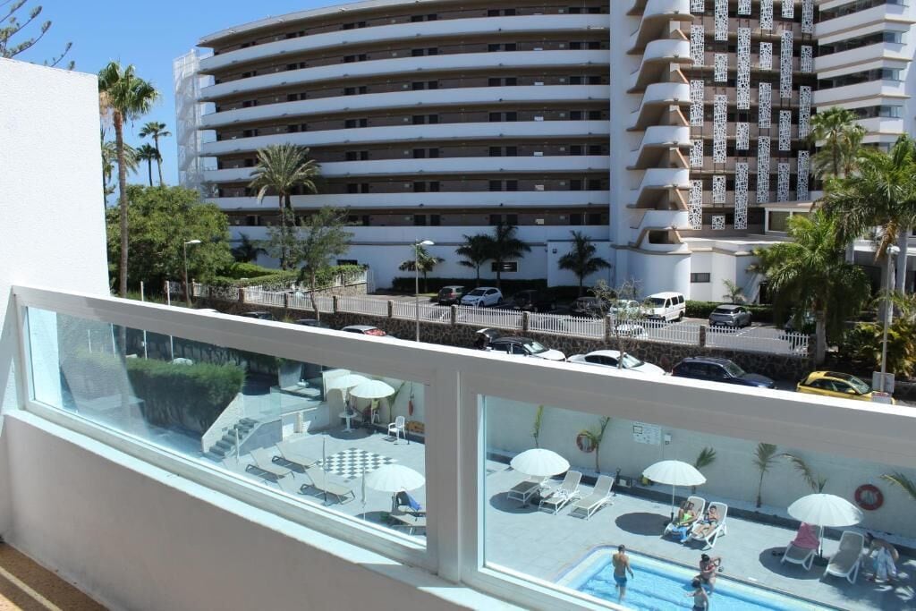 Un hotel con zona de piscina, mobiliario exterior y vistas a un edificio de varios pisos.