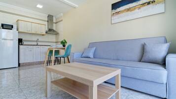 A modern living room with a grey sofa, a wooden coffee table, and a kitchen area with cabinets and a microwave.