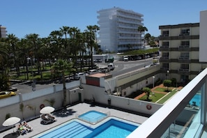 A rooftop pool area with lounge chairs, a pool, and a view of a city street with palm trees and buildings. - Apartamentos Fayna (Gran Canarias)