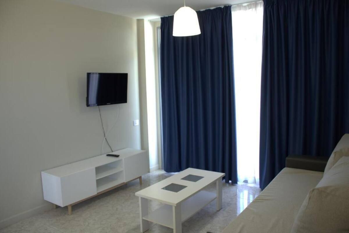 A modern living room with a flat-screen TV, a white coffee table, and a sofa.
