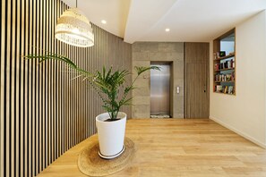 A modern interior with a wooden floor, a white potted plant, a hanging light fixture, and a bookshelf. - Apartamentos Fayna (Gran Canarias)