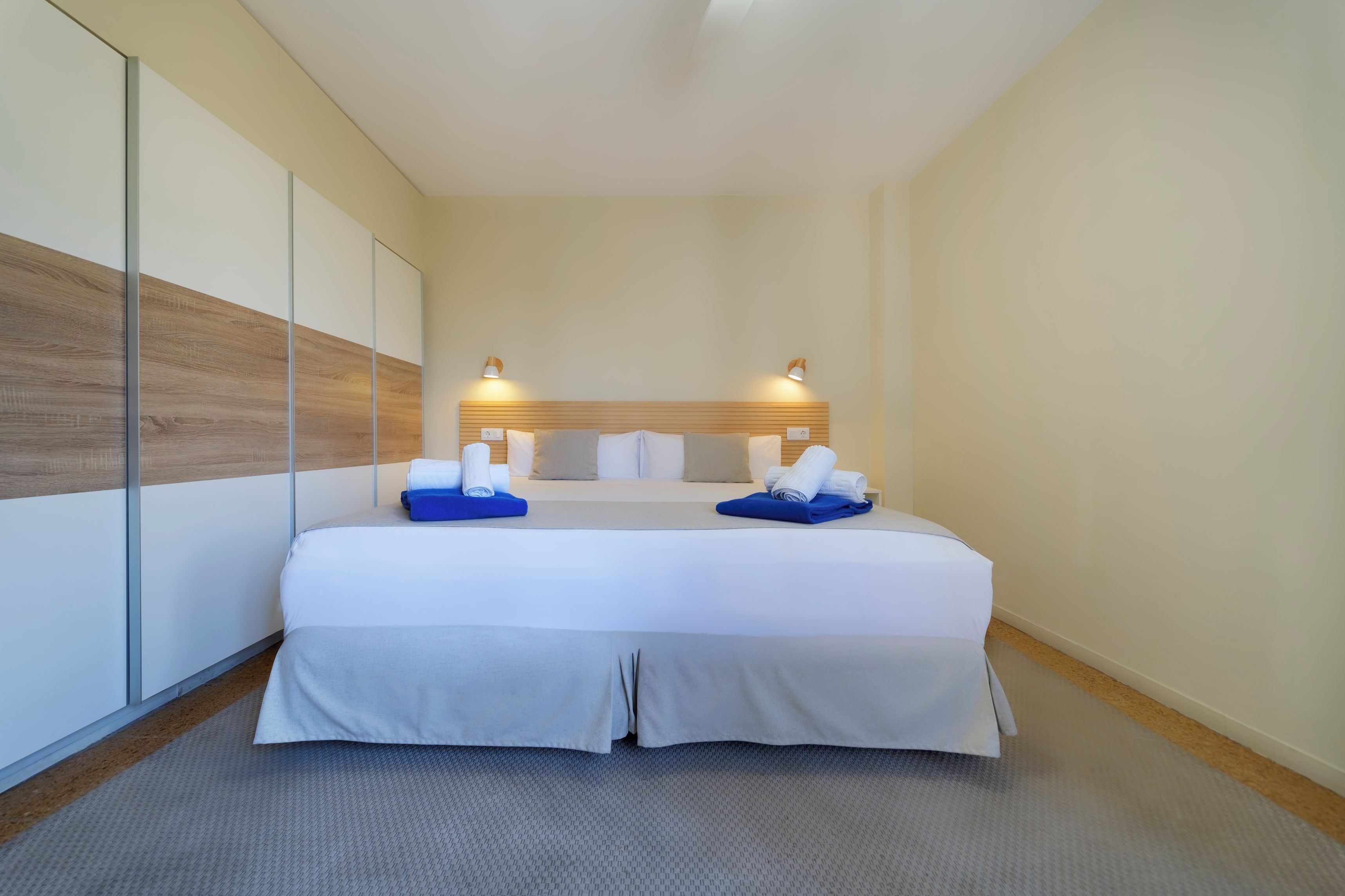 A hotel room with a bed, two bedside tables, a headboard, and a wall-mounted lamp.