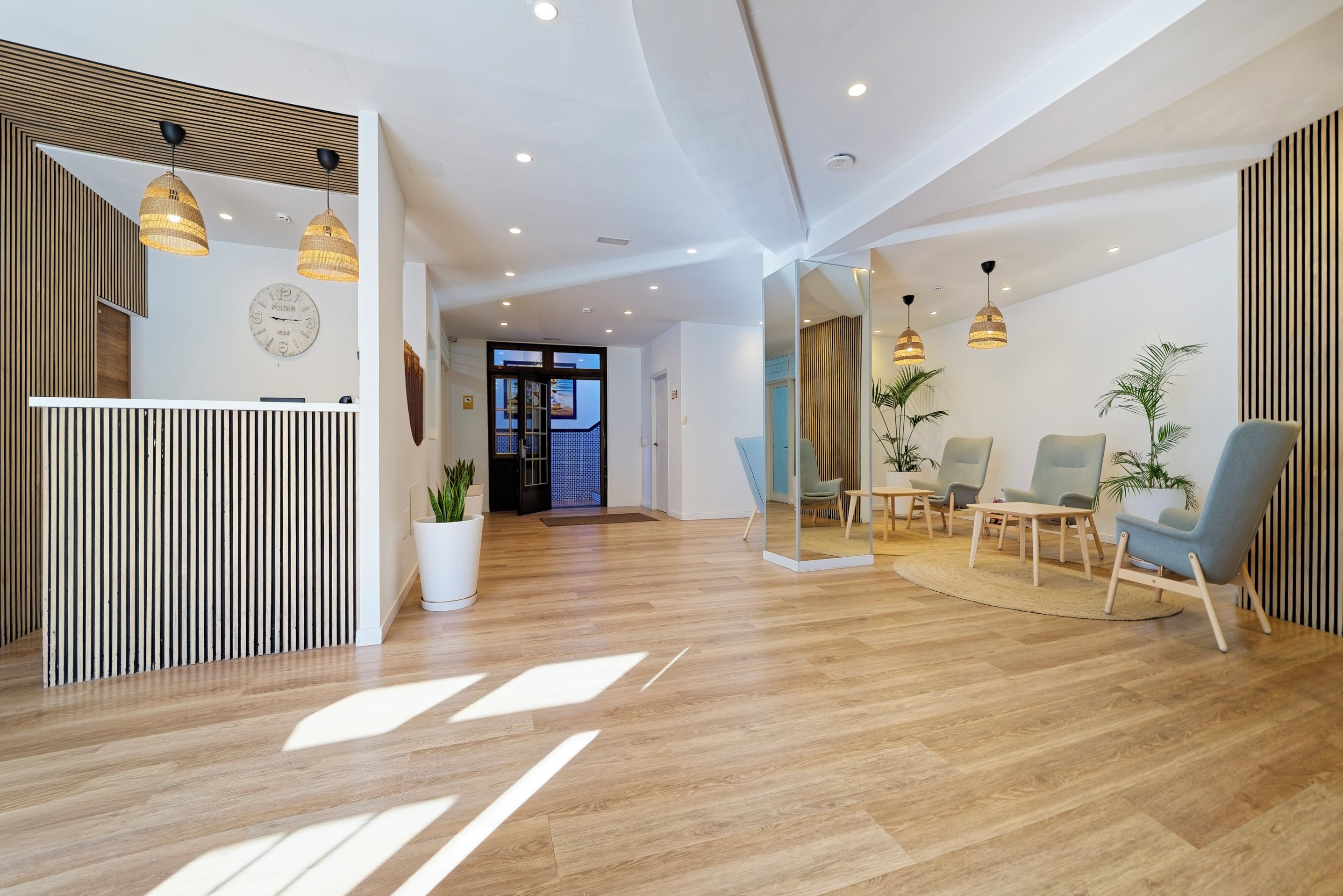 A modern reception area with a wooden reception desk, a wall clock, and a seating area with chairs and a table.