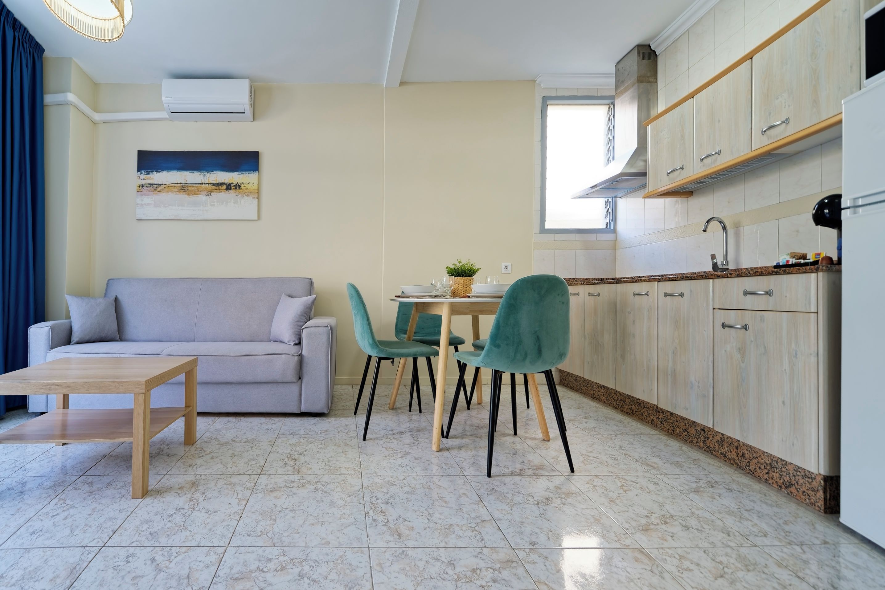 A modern living room with a sofa, a dining table with chairs, and a kitchen area with cabinets and a countertop.