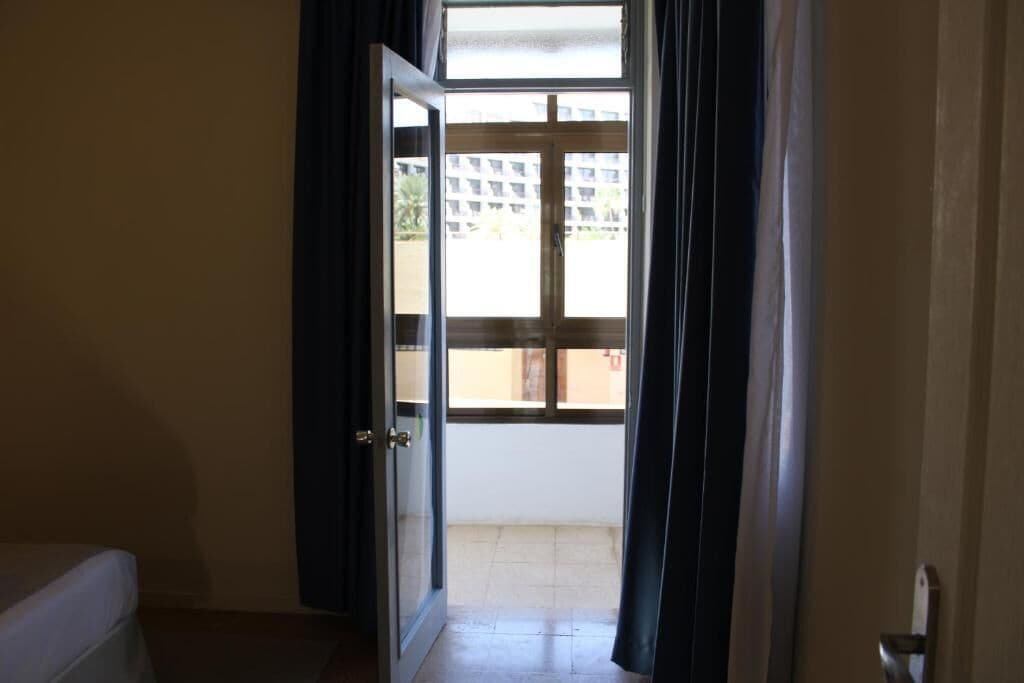 An open door leading to a balcony with a view of a building and a tiled floor.