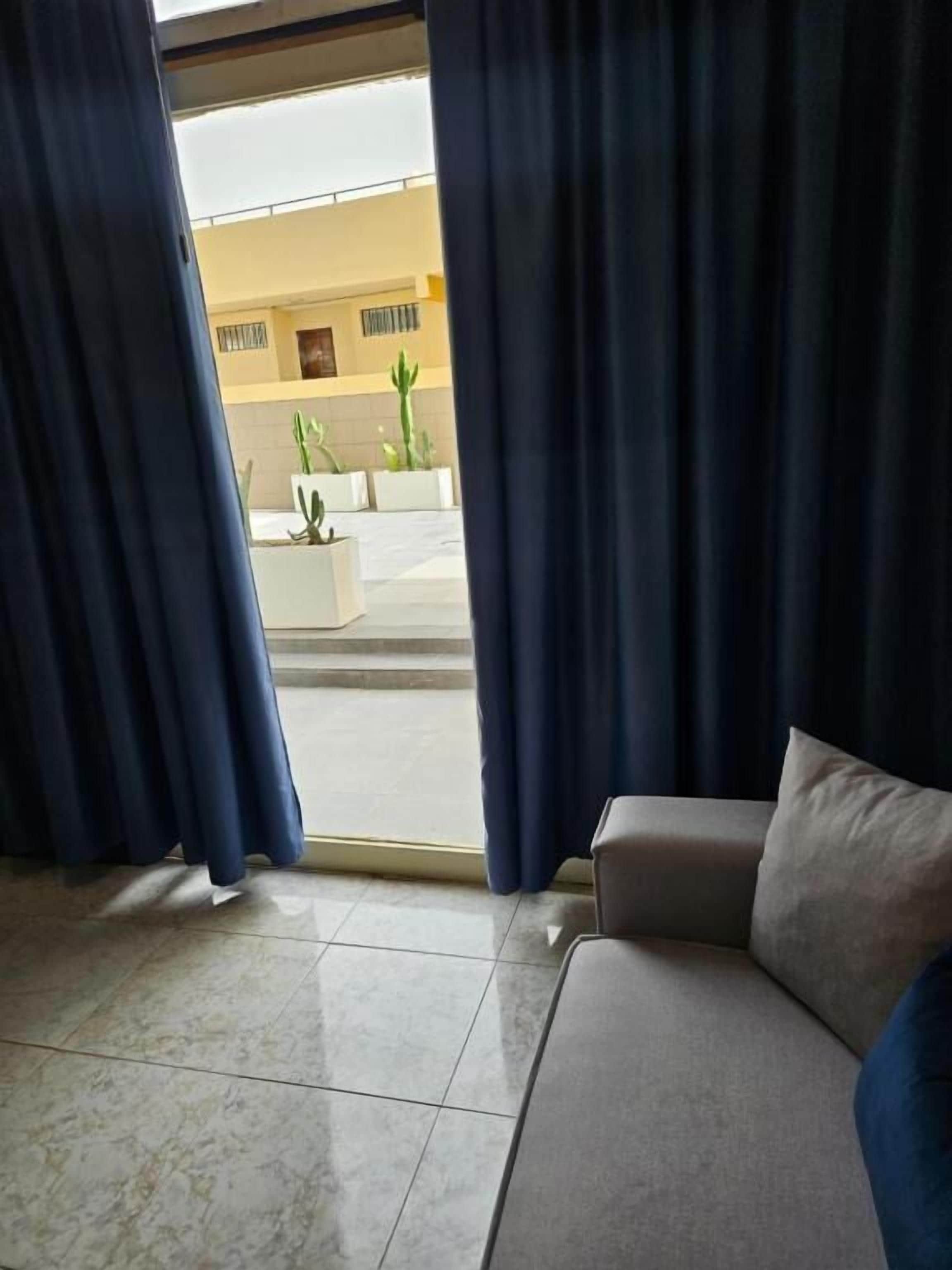 A room with a sofa, a view through a window with curtains, and a tiled floor.