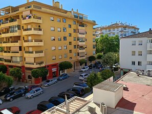 Ein mehrstöckiges gelbes Gebäude mit Balkonen, ein Parkplatz mit verschiedenen Autos und ein weißes Gebäude im Hintergrund.