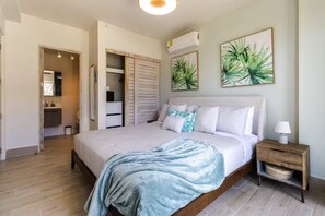 Une chambre à coucher comprenant un lit, une table de chevet, une commode, une armoire et deux unités de climatisation fixées au mur.
