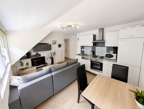 Una cuina moderna amb zona de menjador, un sofà gris i una taula de dinar de fusta.