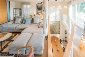 A modern living room with a grey sectional sofa, a wooden dining table, and a staircase leading to an upper level. - Villa Olivo with garden & pool (Montano Lucino)