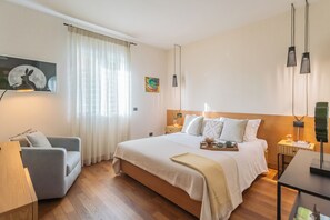 Una camera da letto con un letto, una sedia, una scrivania, una lampada e un quadro appeso al muro.