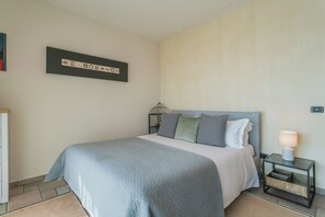 A neatly made bed with a grey blanket, a bedside table with a lamp, and a wall-mounted artwork. - Villa Olivo with garden & pool (Montano Lucino)