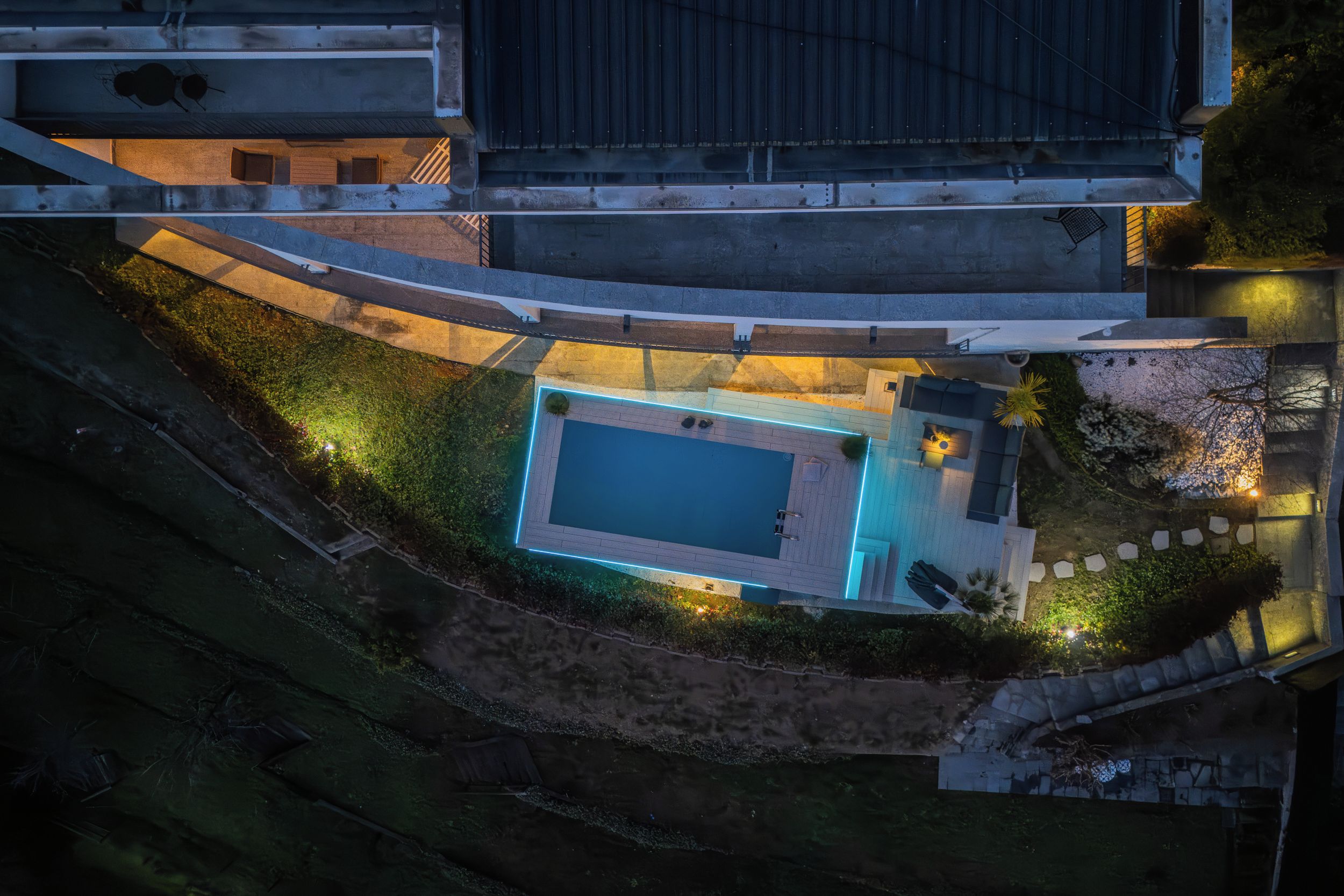 An aerial view of a residential property with a swimming pool, a patio area, and a covered outdoor seating space.