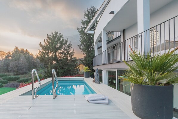 A modern outdoor pool area with a wooden deck, metal railings, and potted plants. - Villa Olivo with garden & pool (Montano Lucino)