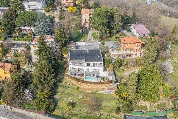Una casa moderna a due piani con un ampio balcone, immersa tra gli alberi e un piccolo giardino.