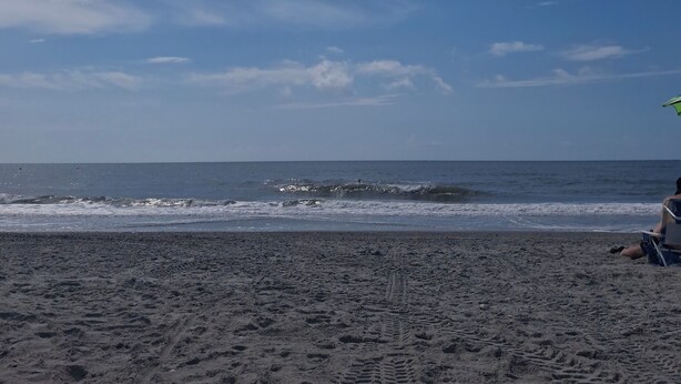 A beach with footprints leading to the water, a clear sky, and a person sitting on a beach chair. - Relax & unwind in a spacious 3-bedroom townhouse with 4 beds in Barefoot Resorts (North Myrtle Beach)
