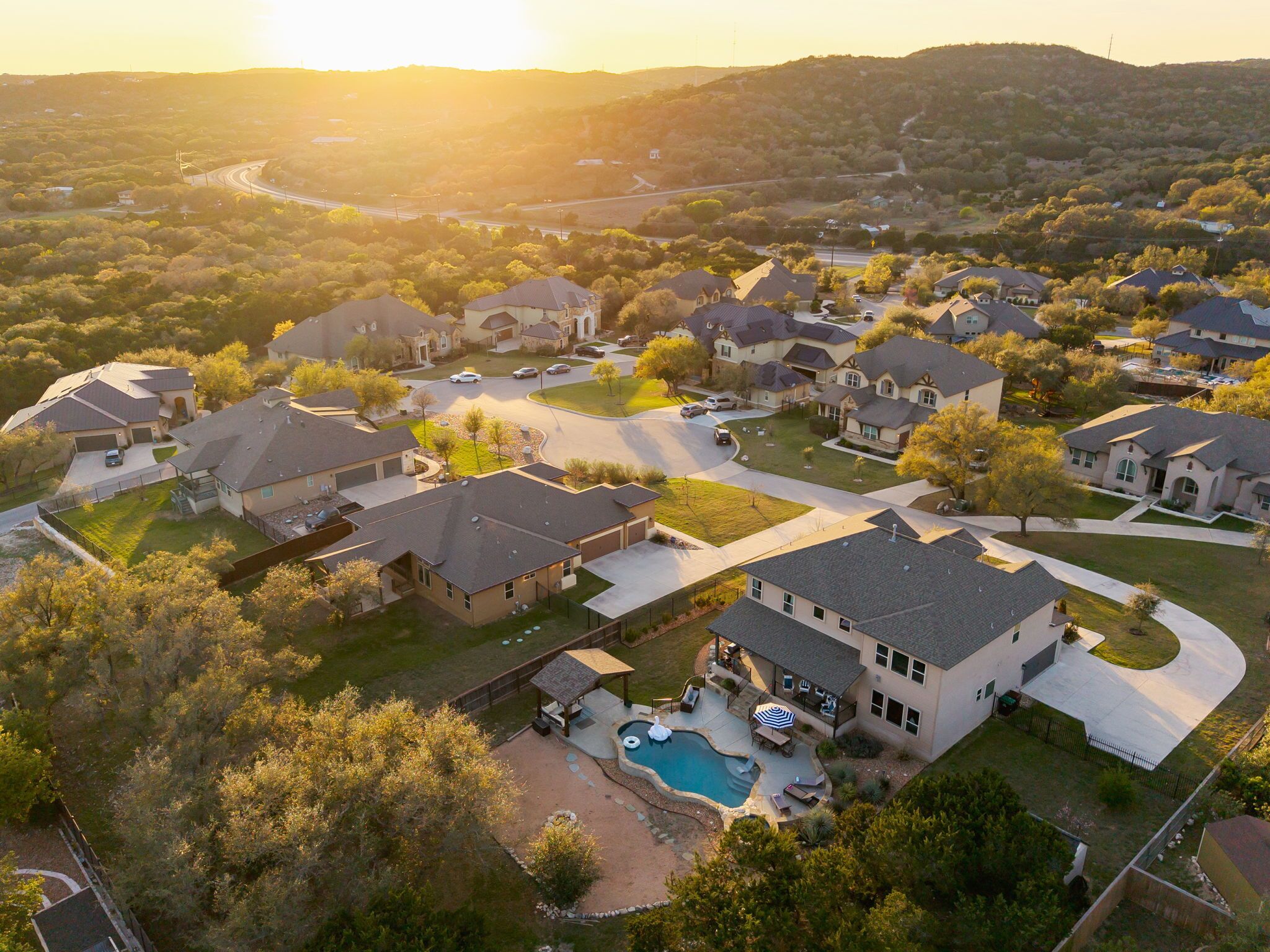 A residential area with houses, a swimming pool, and a hilly landscape in the background.
