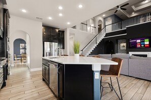 Eine moderne Küche mit Kochinsel, Essbereich mit Stühlen, einer Treppe und einem Wohnbereich mit Sofa und Fernseher.