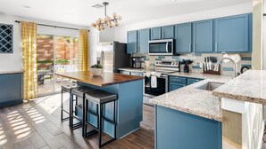 Cocina moderna con armarios azules, una isla central, electrodomésticos de acero inoxidable y vistas a un patio.