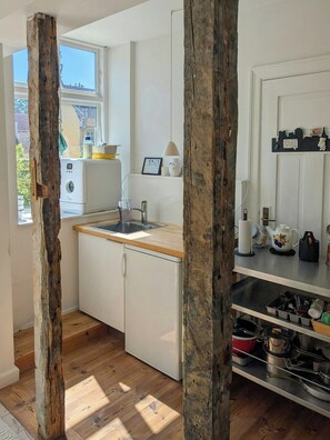 Eine kleine Küche mit Holzbalken, einem Waschbecken, einem weißen Kühlschrank und einem Fenster mit Blick auf Gebäude.