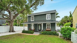 A two-story house with a front porch, a large tree, and a white fence. - Mins to Beaches/Downtown, Quiet Neighborhood, Community Pool (Sarasota)