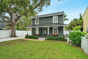 A two-story house with a front porch, a large tree, and a white fence. - Mins to Beaches/Downtown, Quiet Neighborhood, Community Pool (Sarasota)