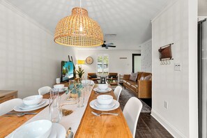 A dining area with a wooden table set for four, white chairs, a large woven pendant light, and a television in the background. - Mins to Beaches/Downtown, Quiet Neighborhood, Community Pool (Sarasota)