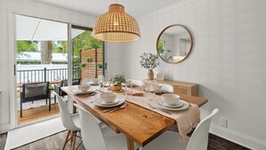 A dining area with a wooden table, white chairs, a hanging light fixture, a round mirror, and a view of the outdoors. - Mins to Beaches/Downtown, Quiet Neighborhood, Community Pool (Sarasota)