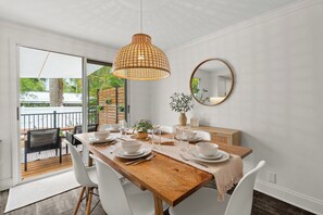 A dining area with a wooden table, white chairs, a hanging light fixture, a round mirror, and a view of the outdoors. - Mins to Beaches/Downtown, Quiet Neighborhood, Community Pool (Sarasota)