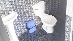 Un baño con inodoro, lavamanos y un cubo de basura azul.