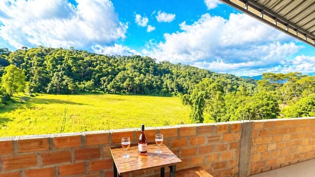 Una terraza con pared de ladrillo, una mesa de madera, dos bancos y una botella de vino.