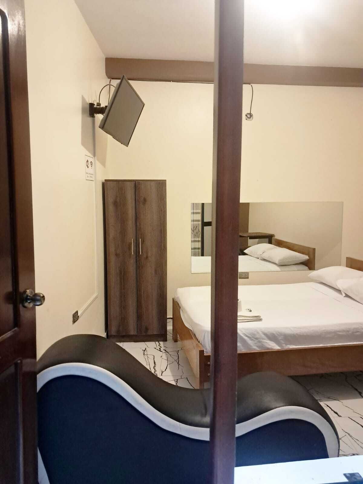 Une chambre à coucher comprenant un lit, une armoire, un miroir et un luminaire fixé au mur.